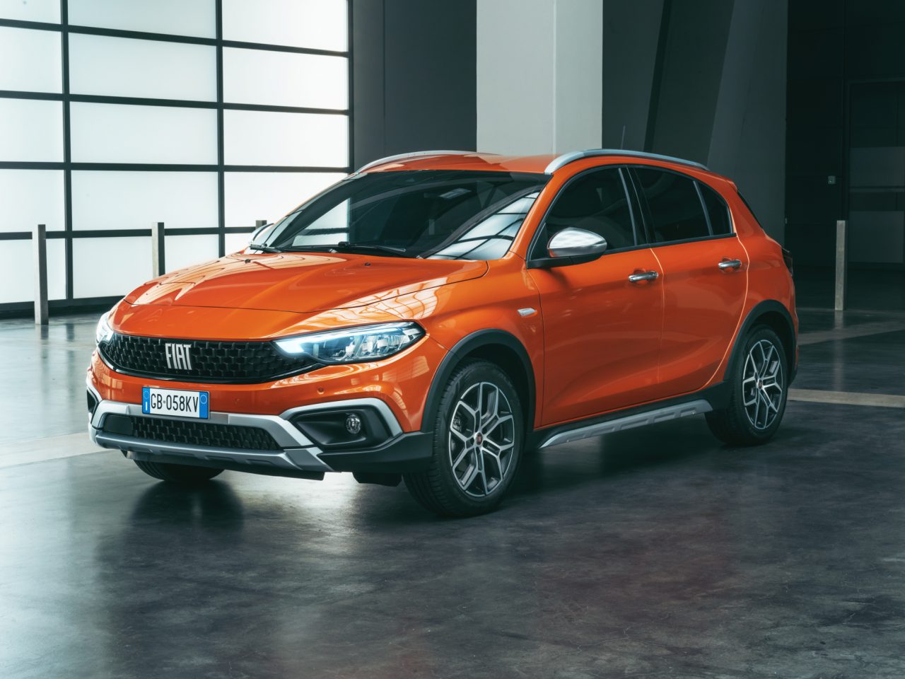 Oranje Fiat Tipo SUV geparkeerd in een ruime, slecht verlichte industriële garage, waar het moderne design en de strakke lijnen goed tot uiting komen.