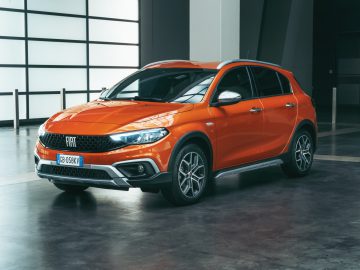 Oranje Fiat Tipo SUV geparkeerd in een ruime, slecht verlichte industriële garage, waar het moderne design en de strakke lijnen goed tot uiting komen.