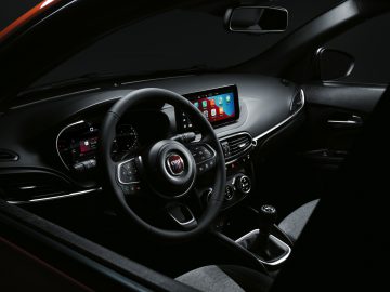 Interieur van een moderne Fiat Tipo-auto met een rood en zwart dashboard, een stuur met logo, digitale displays en handgeschakelde versnellingsbak.