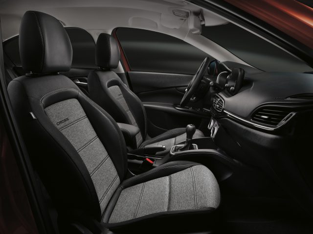 Binnenaanzicht van een Fiat Tipo met een bestuurdersstoel, passagiersstoel en dashboard met modern design en donkere bekleding.