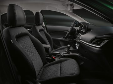Binnenaanzicht van een Fiat Tipo met de bestuurdersstoel, passagiersstoel, stuur en dashboard met bedieningselementen en infotainmentsysteem.