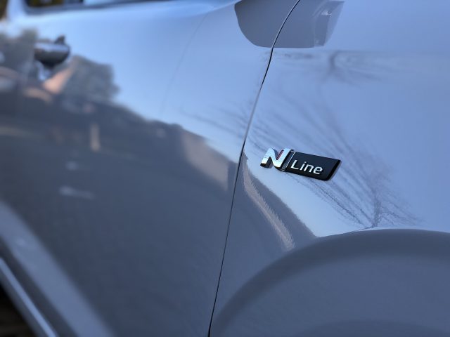 Close-up van het zijpaneel van een Hyundai i10 N Line met het 'n line'-embleem met een wazige straat weerspiegeld op het glanzende oppervlak.