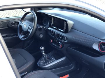 Interieur van een Hyundai i10 N Line met het stuur, de handgeschakelde versnellingsbak en het dashboard met infotainmentscherm.