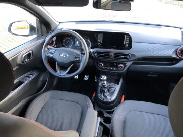 Binnenaanzicht van een Hyundai i10 N Line-auto met het stuur, het dashboard, de middenconsole, de versnellingspook en de voorstoelen.