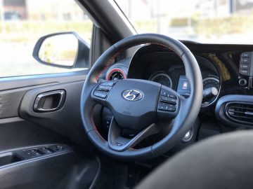 Binnenaanzicht van een Hyundai i10 N Line-auto met het stuur en het dashboard met zichtbare bedieningselementen en instrumenten.