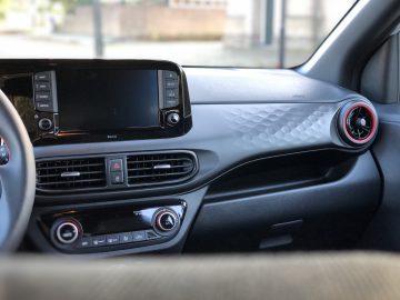 Binnenaanzicht van een Hyundai i10 N Line met een dashboard met touchscreen, ventilatieopeningen en stereobediening, gemarkeerd door een ronde rode ventilatieopening aan de rechterkant.