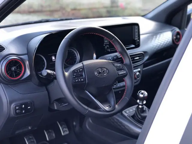 Binnenaanzicht van een auto met een stuur met het Hyundai i10 N Line-logo, dashboard, versnellingspook en bestuurdersdeur.