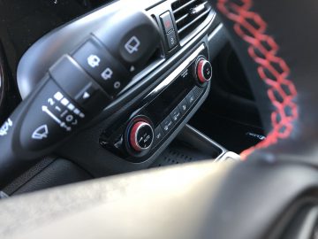 Close-up van het stuur en het dashboard van een Hyundai i10 N Line, waarbij de nadruk ligt op de bedieningselementen en de knoppen met rode accenten.