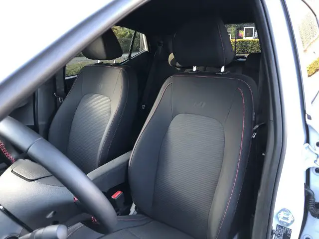 Binnenaanzicht van een Hyundai i10 N Line met de voorstoelen en deur, met zwarte bekleding en rode stiksels.