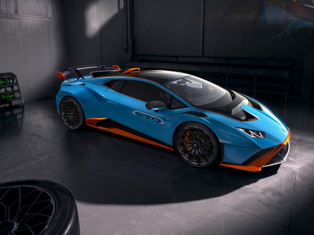 Een blauwe Lamborghini Huracán STO met oranje accenten geparkeerd in een slecht verlichte garage, die het strakke ontwerp en de aerodynamische kenmerken laat zien.