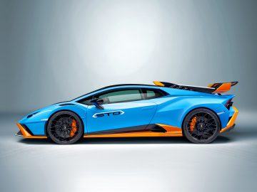 Blauw-oranje Lamborghini Huracán STO geparkeerd in een studio met een spotlight die het strakke ontwerp benadrukt.