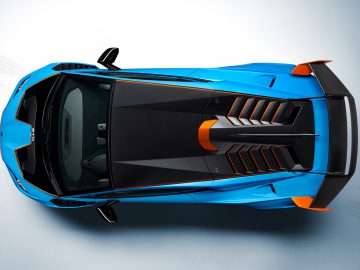 Van bovenaf gezien een blauwe Lamborghini Huracán STO met zwarte details, geparkeerd op een grijs gestructureerd oppervlak.