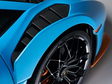 Close-up van een blauwe Lamborghini Huracán STO met het achterwiel en het spatbord met zichtbare koolstofvezeldetails en oranje remklauwen.
