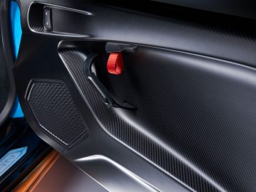 Close-up van het interieur van een Lamborghini Huracán STO-autodeur met koolstofvezelpanelen, een geïntegreerde luidspreker en een opvallende rode deurgrendel.