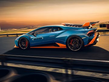 Een blauw-oranje Lamborghini Huracán STO die tijdens zonsondergang te hard rijdt op een racecircuit.