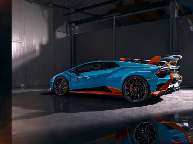 Een blauwe Lamborghini Huracán STO geparkeerd in een slecht verlichte garage, reflecterend op een gepolijste betonnen vloer.