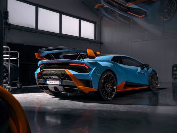 Blauw en oranje Lamborghini Huracán STO geparkeerd in een garage met gereedschap en auto-onderdelen zichtbaar op de achtergrond.