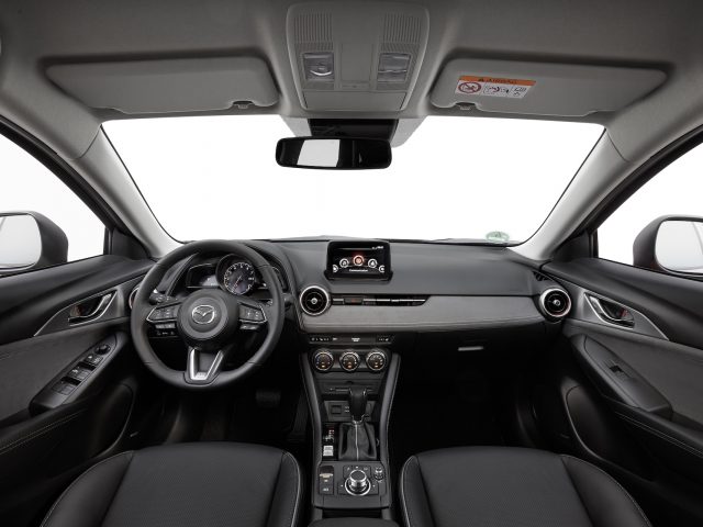 Binnenaanzicht van een Mazda CX-3, met het stuur, het dashboard, de middenconsole en de voorstoelen, allemaal in het zwart.