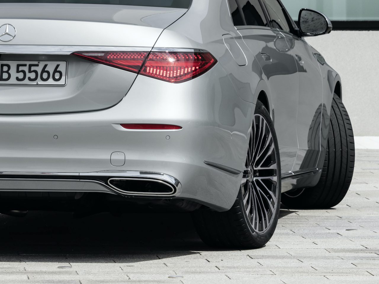 Achteraanzicht van een zilveren Mercedes-Benz S-Klasse met de achterlichten, de kofferbak en de kentekenplaat, geparkeerd op een betonnen ondergrond nabij een gebouw.