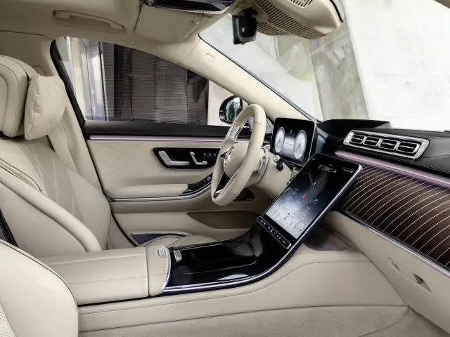 Binnenaanzicht van een Mercedes-Maybach S-Klasse met een crèmekleurig lederen interieur, een groot touchscreen op de middenconsole en elegante houten lambrisering.