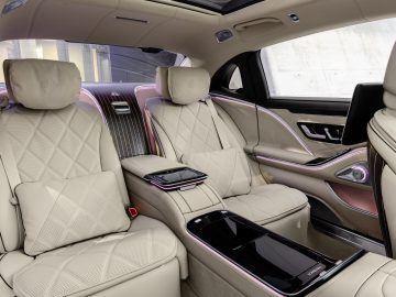 Binnenaanzicht van een Mercedes-Maybach S-Klasse met de ruime achterbank met crèmekleurige lederen bekleding, sfeerverlichting en moderne digitale consoles.