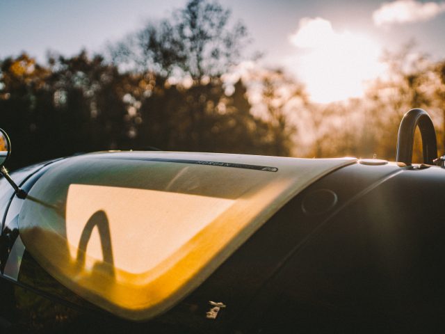 Zonsonderganglicht dat weerkaatst op de voorruit en motorkap van een Morgan 3 Wheeler en toont een wazige herfstboomachtergrond.