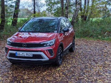 De Opel Crossland parkeerde op een met bladeren bedekt pad met bomen op de achtergrond, een natte ondergrond die wijst op recente regen.