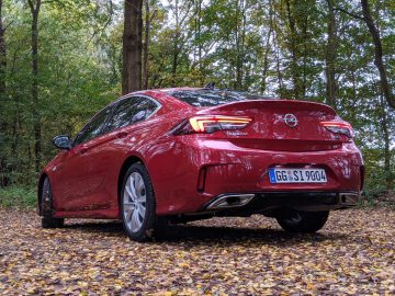 Rode Opel Insignia geparkeerd op een met bladeren bedekt pad in een bos tijdens de herfst.