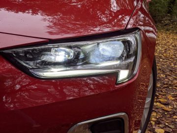 Close-up van de koplamp van een Opel Insignia die aanstaat en reflecteert tegen een achtergrond van natte herfstbladeren.