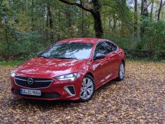 Opel Insignia sedan geparkeerd op een met bladeren bedekte weg in een bos tijdens de herfst.