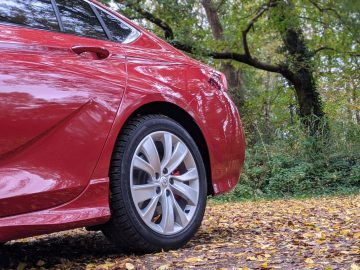 Een rode Opel Insignia geparkeerd op een met bladeren bedekt pad met een achtergrond van bomen in de herfst.
