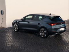 Donkergrijze Seat Leon e-Hybrid opladen bij een aan de muur gemonteerd laadstation op een gladde betonnen oprit.