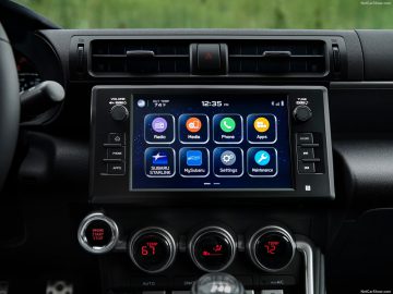 Autodashboard van een Subaru BRZ met een touchscreen-infotainmentsysteem met pictogrammen voor radio, media, telefoon, apps, instellingen en onderhoud, geflankeerd door klimaatknoppen.