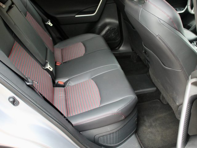 Binnenaanzicht van een Suzuki Across Plug-in Hybrid, waarbij de achterbank is bekleed met grijs en rood gestreepte stof, met zichtbare deur- en vloerdetails.
