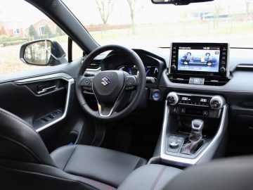 Binnenaanzicht van de Suzuki Across Plug-in Hybrid, met het stuur, het dashboard en het infotainmentsysteem met twee schermen.