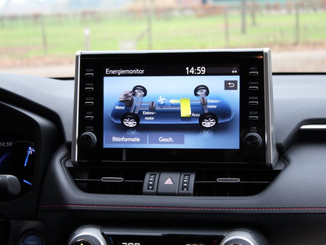 Een digitaal display in een Suzuki Across Plug-in Hybrid met een energiemonitor, met grafische weergaven van motor- en batterijfuncties, bekeken bij daglicht.