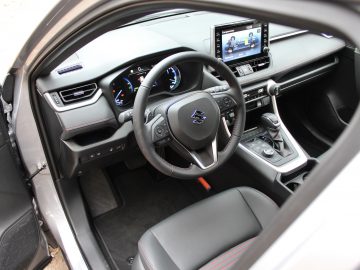 Binnenaanzicht van een Suzuki Across Plug-in Hybrid vanaf de bestuurderszijde met een stuur met logo, dashboard en multimediasysteem.
