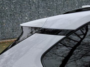 Close-up van het glanzend witte dak van een Suzuki Across Plug-in Hybrid met een panoramisch zonnedak, met strakke lijnen en gereflecteerde bomen op het glanzende oppervlak.