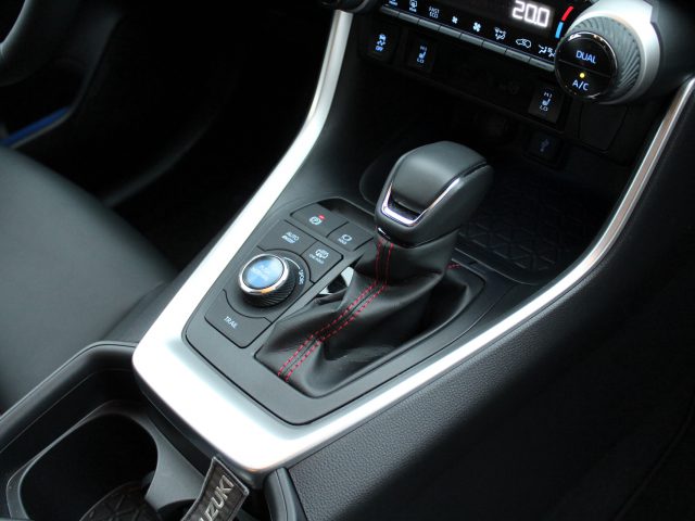 Binnenaanzicht van een Suzuki Across Plug-in Hybrid met een automatische versnellingspook, bekerhouders en klimaatregelingsknoppen.