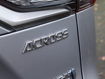 Close-up van het grijze achterpaneel van een Suzuki Across Plug-in Hybrid met de modelnaam "across" in verhoogde zilveren letters.