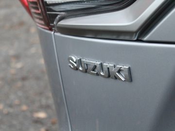 Close-up van de achterkant van een grijze Suzuki Across Plug-in Hybrid met de merknaam in verhoogde zilveren letters op de carrosserie.