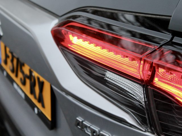 Close-up van het verlichte achterlicht van een Suzuki Across Plug-in Hybrid, met een wazig Brits kenteken op de achtergrond.