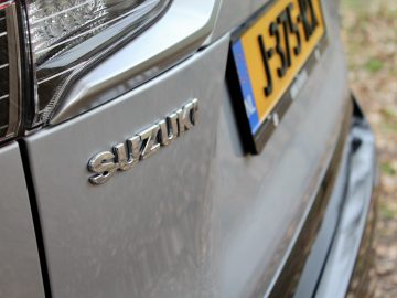 Close-up van de grille van een zilveren Suzuki Across Plug-in Hybrid-auto met een zichtbaar merkembleem en gedeeltelijk zicht op de kentekenplaat.