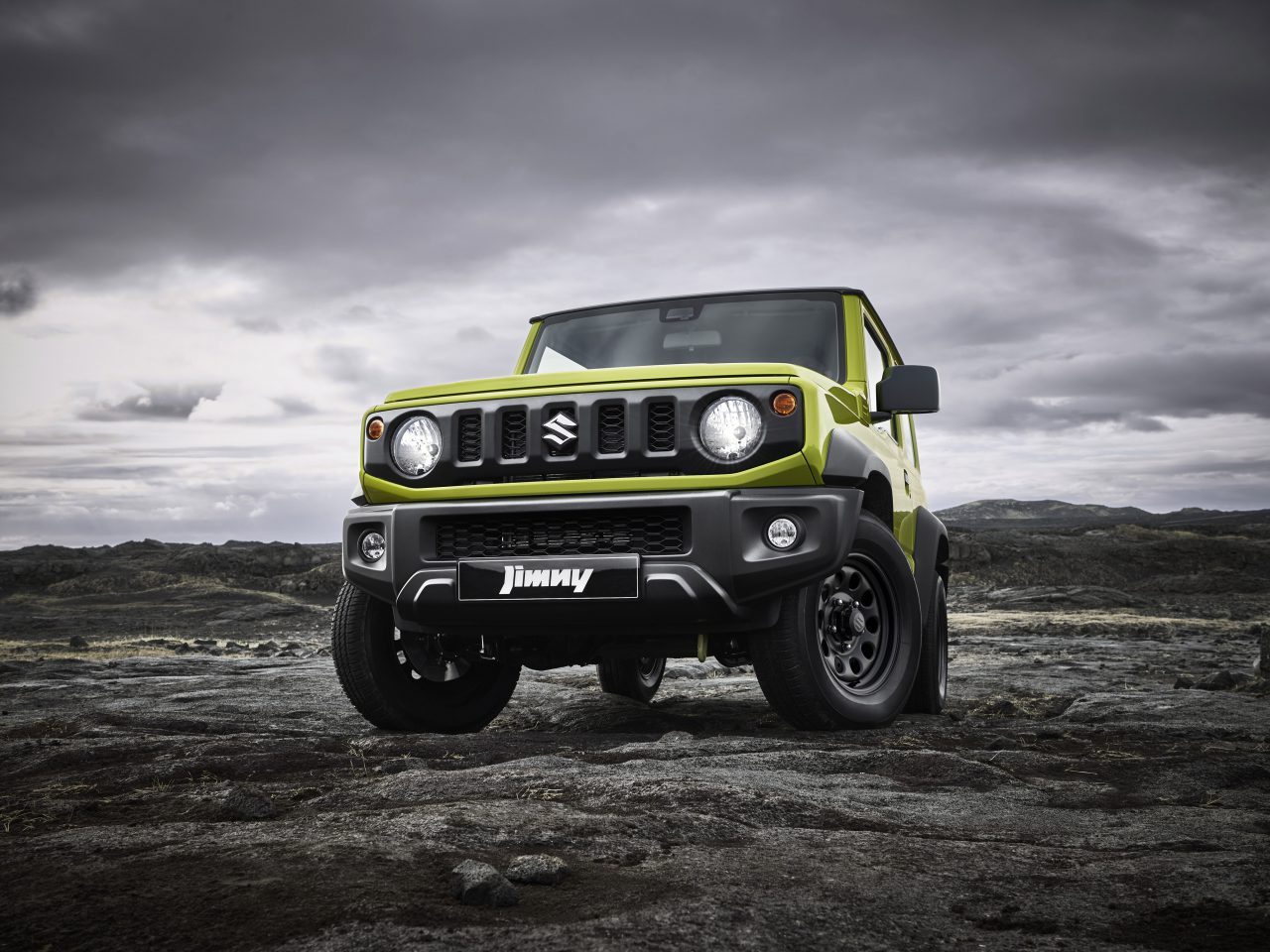Een felgroene Suzuki Jimny Professional geparkeerd op een rotsachtig terrein onder een stormachtige lucht.