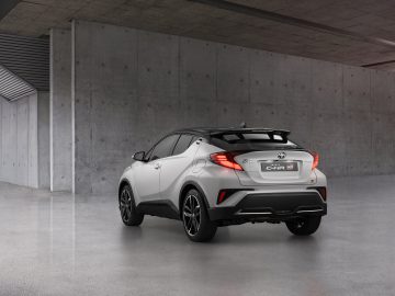 Een zilveren Toyota C-HR GR-Sport geparkeerd in een betonnen gebouw, gezien vanuit de rechter achterhoek, wat het strakke ontwerp en de zwarte sierdetails benadrukt.