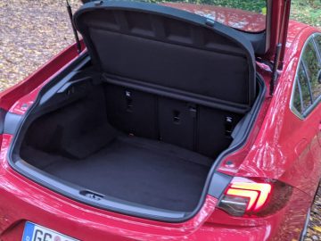 Open kofferbak van een rode Opel Insignia met lege laadruimte, buiten geparkeerd met bomen op de achtergrond.
