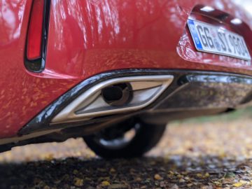 Close-up van de achterste uitlaat en bumper van een rode Opel Insignia, met een onscherpe achtergrond van gevallen bladeren en een zichtbare kentekenplaat.