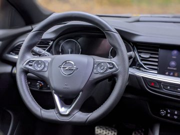 Binnenaanzicht van een Opel Insignia met een gedetailleerd stuur met Opel-logo en dashboard op een zachte focusachtergrond.