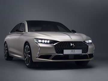 Een zilveren DS 9 e-tense-auto tentoongesteld in een studioomgeving, met zijn strakke ontwerp en opvallende grille aan de voorkant.