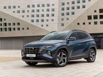 Een Hyundai Tucson SUV geparkeerd voor een modern gebouw met een geometrische witte gevel.